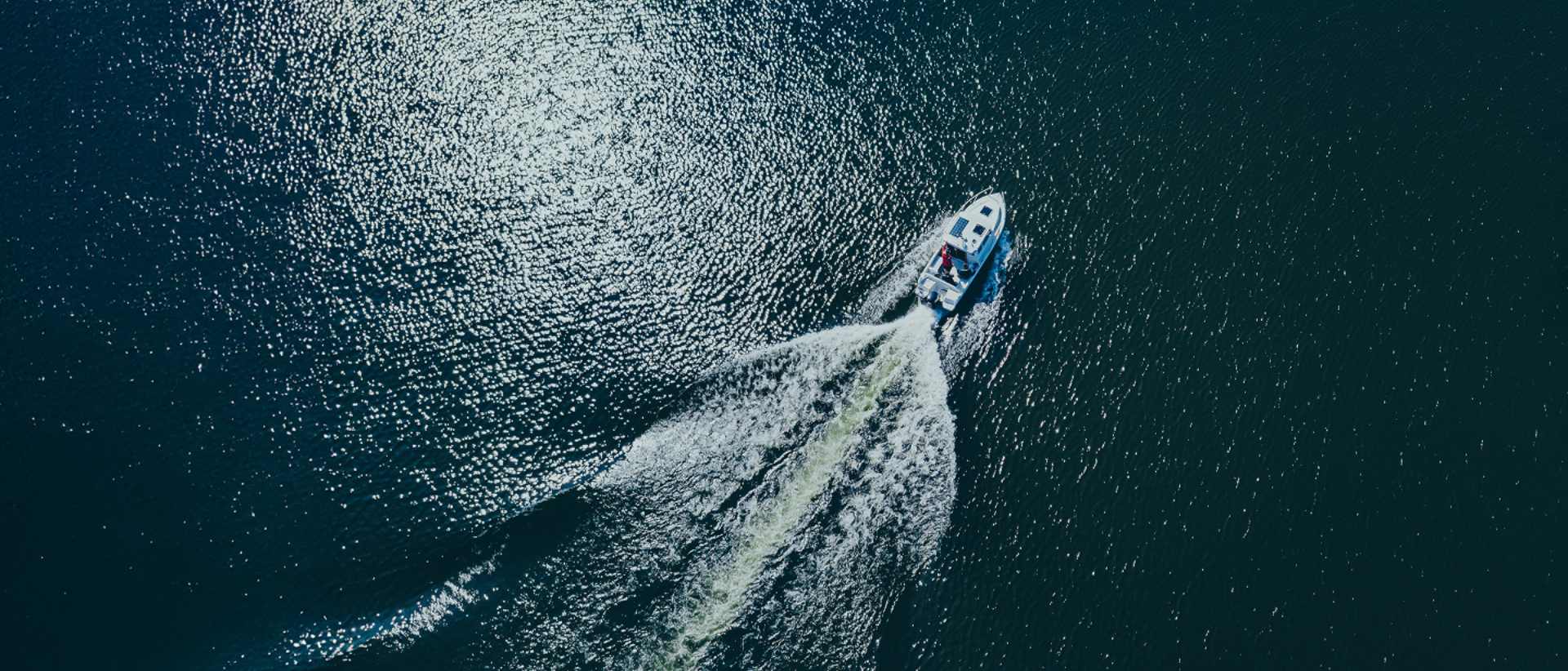 An electric boat navigating the ocean, creating waves, with a silent electric motor aerial view